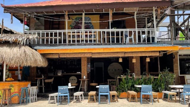 Two-story beachside café in Siargao with colorful chairs and tables outside, under a red roof and wooden balcony.