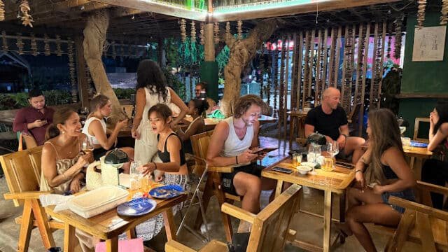 People dining and chatting at a lively, rustic Siargao restaurant with wooden tables and warm lighting.