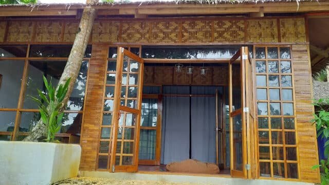 A wooden bungalow with glass doors, bamboo walls, and a plant by the entrance in scenic Siargao.