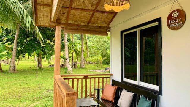 Cozy porch with a bench, cushions, wooden table, and lush Siargao greenery in the background at Bloom Siargao.