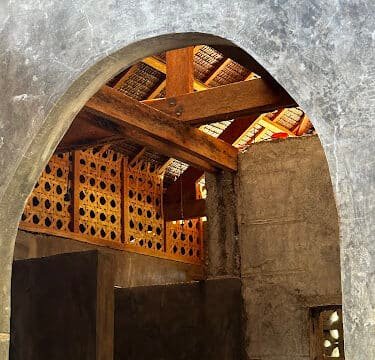 Sunlight shines through a wooden roof and lattice above a stone archway inside a rustic Siargao building.