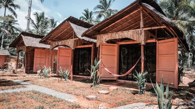 Three bamboo huts with open doors, surrounded by palm trees on Siargao, and a red hammock hanging in front.