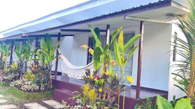 Single-story white house with a porch, hammock, and lush tropical plants—perfect for relaxing Siargao vibes in the garden.