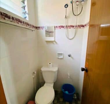 Cozy Siargao bathroom with a toilet, blue bucket, showerhead, and water heater on a tiled floor.