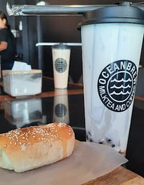 A sesame-topped bread roll and Oceanbrew bubble tea on a wooden tray in a cozy Siargao cafe.