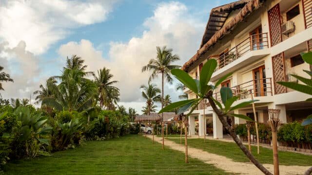 Tropical Siargao hotel with a balcony, palm trees, and a grassy lawn under a partly cloudy sky.