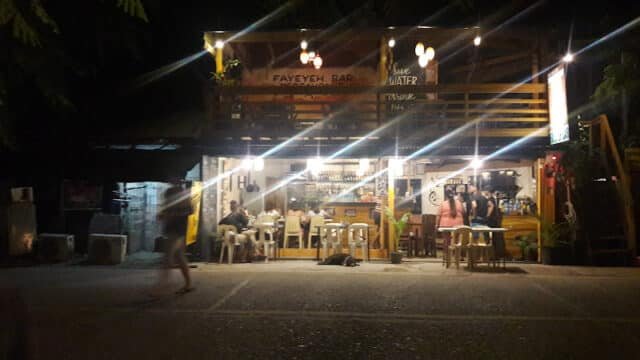 A cozy, warmly lit bar in Siargao with people sitting at tables outside at night.
