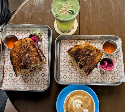 Two grilled sandwiches with sauces, a matcha drink, and a latte with art on a round brown table in Siargao.