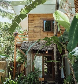 A cozy wooden house in Siargao, surrounded by lush tropical plants and swaying palm trees.