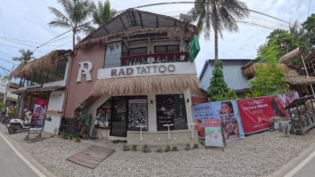 A two-story building with RAD TATTOO signage, palm trees, and a banner for tattoo services in Siargao outside.