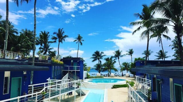 Siargao resort with blue buildings, palm trees, pools, and stunning ocean views under a bright blue sky.