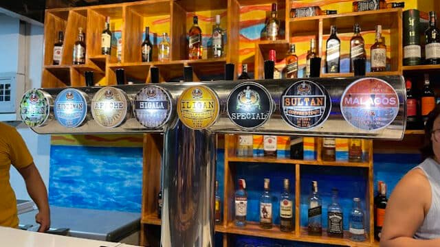 Beer taps labeled with various local brews at a colorful Siargao bar, bottles displayed on wooden shelves behind.