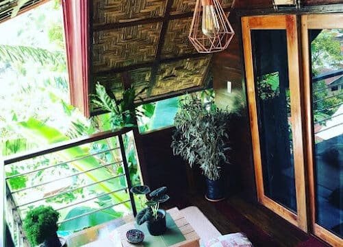Cozy Siargao balcony with plants, a low table, floor cushions, and glass doors, surrounded by lush greenery.