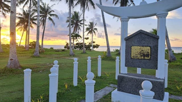 A stone monument with a plaque, surrounded by palm trees, stands near the Siargao ocean at sunset.