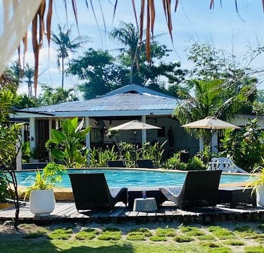 Lounge chairs by a pool with umbrellas, surrounded by greenery and a tropical Siargao villa in the background.