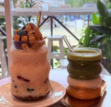 Two colorful drinks in wavy glasses on a table by a window, with lush Siargao greenery and outdoor scenery in the background.