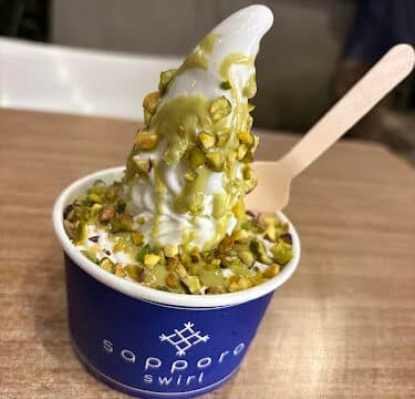 A cup of soft-serve ice cream topped with chopped pistachios in a blue Sapporo Swirl cup on a Siargao table.