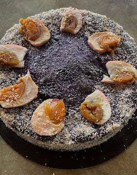 Round purple Siargao cake topped with sliced dried fruit, surrounded by grated coconut on a dark surface.