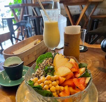 A bowl of salad with chickpeas, apples, tomato, and quinoa sits beside drinks on a wooden café table in Siargao.