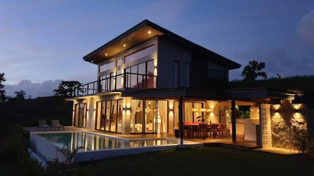 Modern two-story house with large windows, outdoor pool, and warm lighting at dusk—perfect for a relaxing Siargao retreat.