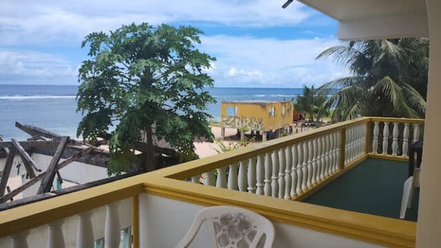 View from a balcony overlooking the ocean, palm trees, and a yellow building under Siargao's cloudy blue sky.