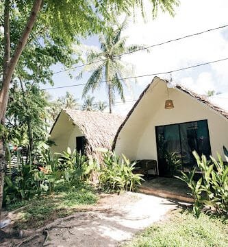 Two thatched-roof huts in Siargao, surrounded by lush greenery and palm trees on a sunny day.