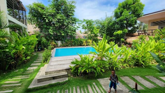 A small pool surrounded by lush greenery in Siargao, with a child walking on a stone path in the foreground.