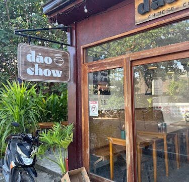 A scooter parked outside Dao Chow restaurant in Siargao, with large windows, a wooden sign, and green plants nearby.