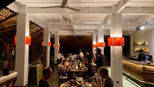 People dining inside a warmly lit Siargao restaurant with wooden decor and red lampshades, some are eating and talking.
