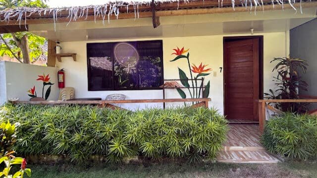 A Siargao bungalow with a wooden door, mural of flowers, patio chairs, and lush green plants in front.