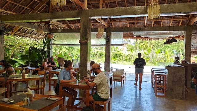 Open-air café with wooden tables, people dining, and lush Siargao greenery visible outside on a sunny day.