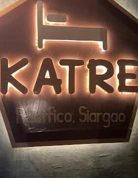 Illuminated sign with a bed icon and the text KATRE, Pacifico, Siargao, adds charm to your stay in Siargao.