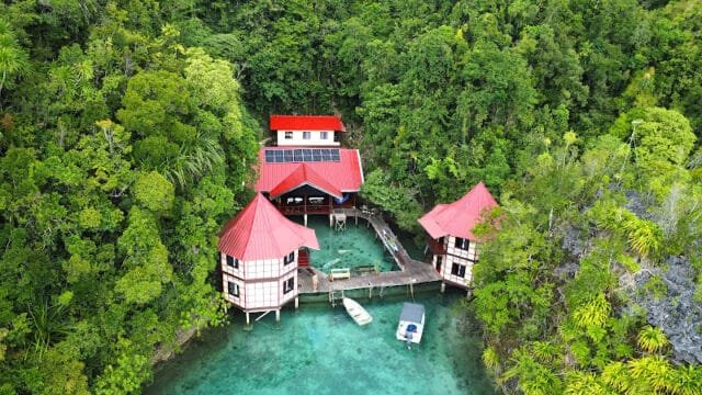 Aerial view of red-roofed overwater bungalows in Siargao, surrounded by lush green forest and turquoise water.