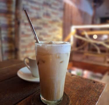 A glass of iced coffee with a metal straw on a coaster, set on a wooden table in a cozy Siargao cafe.