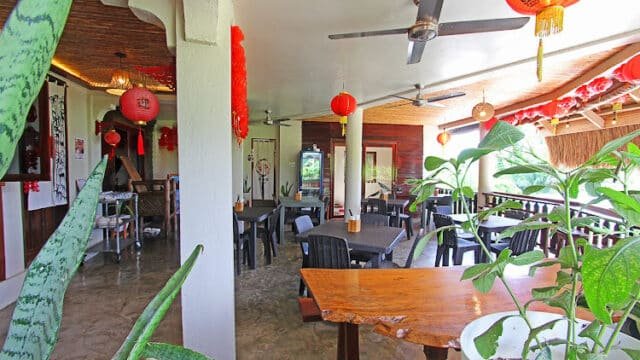 Open-air Siargao restaurant with Chinese lanterns, ceiling fans, black chairs, and potted plants on tables and ledges.