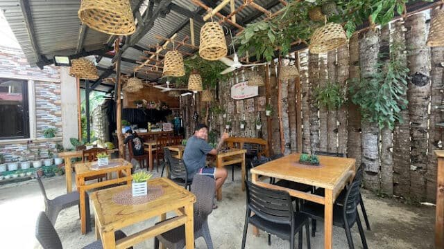 Cozy outdoor café in Siargao with wooden tables, hanging wicker lamps, and a person waving at the camera.