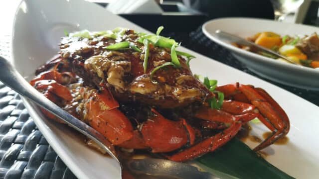Cooked crab with sauce and green garnish, served Siargao-style on a white plate, with a spoon on the side.