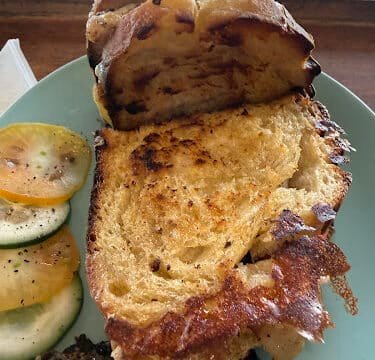 Grilled sandwich on a plate with sliced yellow tomatoes and Siargao-fresh cucumbers on the side.
