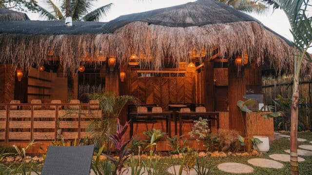 A tropical outdoor restaurant in Siargao with a thatched roof, wooden furniture, and lush plants surrounding the area.