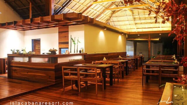 A warmly lit, modern wooden restaurant interior in Siargao with neatly arranged tables and chairs under a thatched roof.
