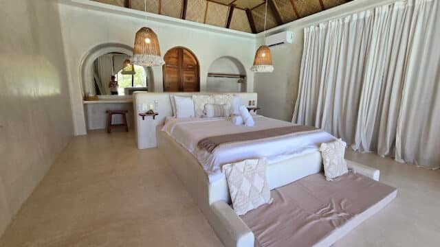 A spacious, modern Siargao bedroom with a large bed, neutral tones, woven lamps, and white curtains.