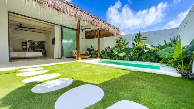 Open villa with thatched roof in Siargao, green lawn, pool, tropical plants, and a blue sky with white clouds.