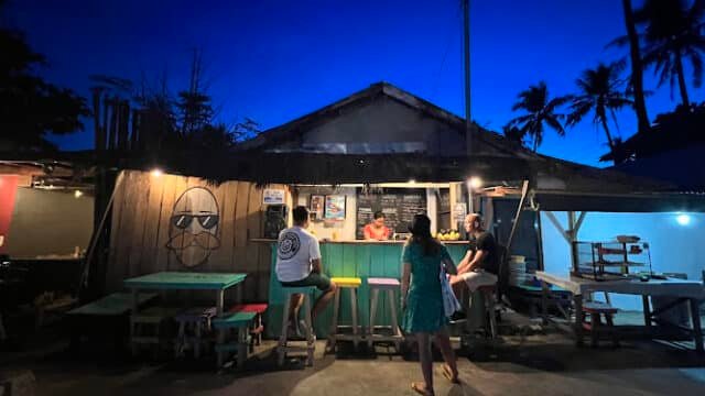 Outdoor food stall at dusk in Siargao, with people ordering under a deep blue sky and palm trees in the background.