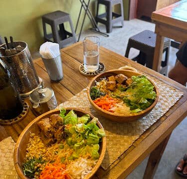 Two bowls of colorful noodle salads with veggies on a wooden table in a cozy Siargao cafe setting.
