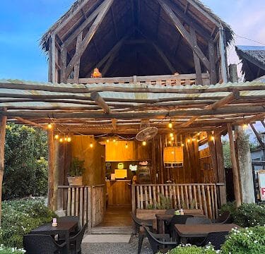 Cozy, rustic cafe in Siargao with outdoor seating, warm string lights, and a thatched roof at dusk.