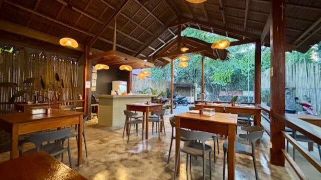 Open-air Siargao restaurant with wooden tables and chairs, warm lighting, a thatched roof, and an inviting evening setting.