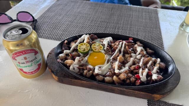 A sizzling plate of pork sisig with egg and calamansi, perfect for enjoying with a San Miguel flavored beer after surfing in Siargao.