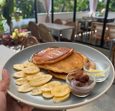 A plate of pancakes with sliced bananas, syrup, and chocolate sauce enjoyed at a sunny Siargao outdoor café.
