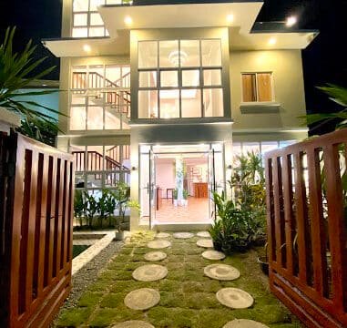 Modern three-story house at night with large windows, lit exterior, and a stone path weaving through a Siargao-inspired garden.