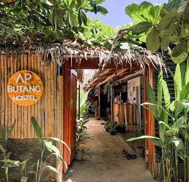 Entrance to AP Butang Hostel in Siargao with bamboo walls, tropical plants, and a sandy path leading inside.